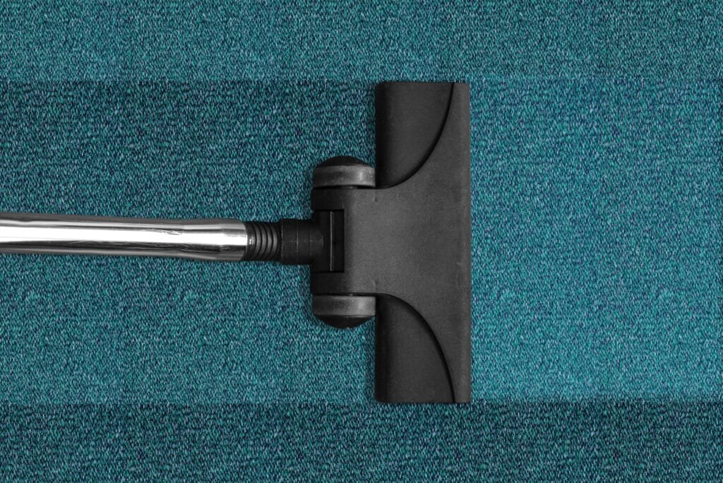 A vacuum cleaner head is shown cleaning a teal carpet in a San Jose commercial space, leaving a visibly cleaner stripe behind—ideal for post-construction cleaning.