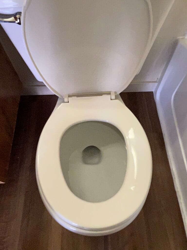 Overhead view of an open, clean white toilet with the seat and lid raised, placed on a brown wooden floor next to a bathtub—ideal inspiration for bathroom deep cleaning or targeting commonly missed bathroom areas.