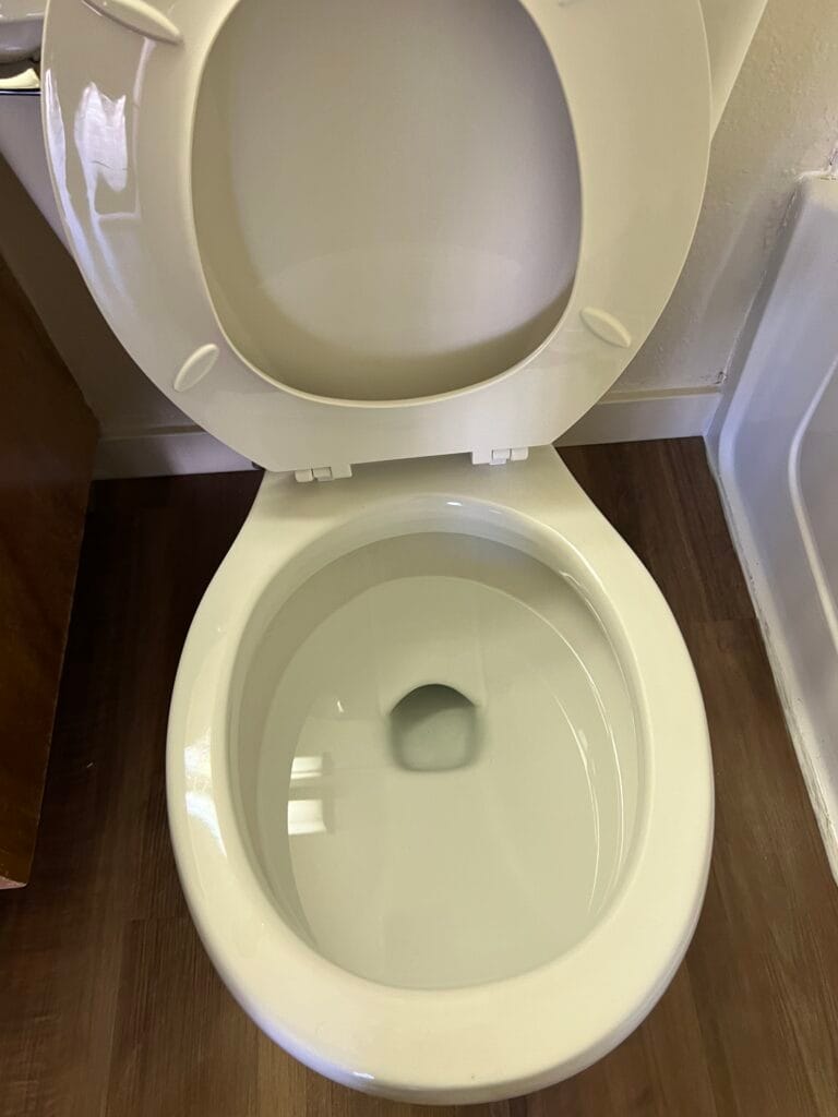 An open, clean white toilet with the lid raised, situated on a wooden floor next to a white bathtub—a testament to meticulous bathroom deep cleaning every homeowner appreciates.