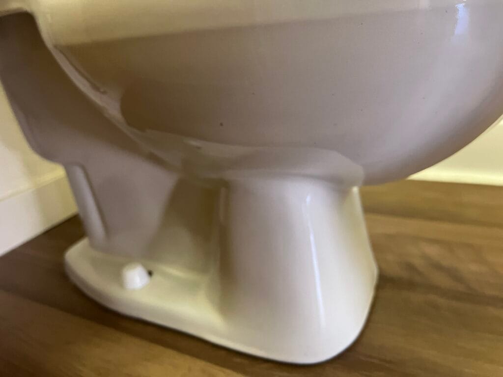Close-up view of the base of a white ceramic toilet set against a brown wooden floor—showcasing the attention to detail homeowners seek during bathroom deep cleaning.