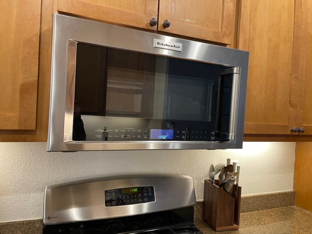 Perfect for busy families, this stainless steel KitchenAid microwave is mounted above the stove in a Los Gatos kitchen, surrounded by wooden cabinets and a utensil holder on the right side of the countertop.