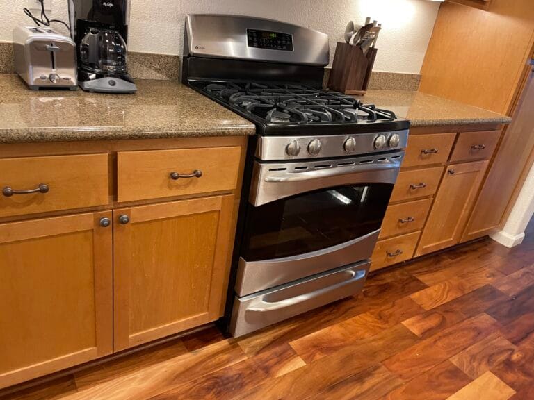 A stainless steel gas stove with an oven is installed between wooden cabinets and drawers in a Los Gatos kitchen with brown countertops and wood flooring—perfect for busy families needing kitchen deep cleaning.